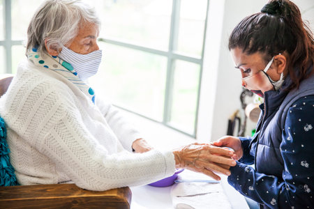 Senior woman getting a manicure at home during Covid-19 pandemic wearing face maskの写真素材