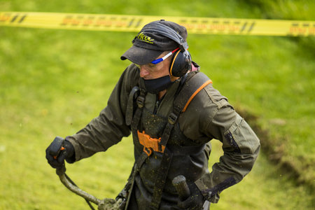 LA CALERA, COLOMBIA - MAY, 2020: Man scything wearing safety personal protective equipment and face...