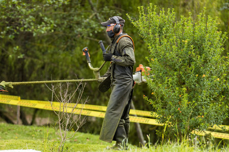 LA CALERA, COLOMBIA - MAY, 2020: Man scything wearing safety personal protective equipment and face mask during the  coronavirus pandemicのeditorial素材