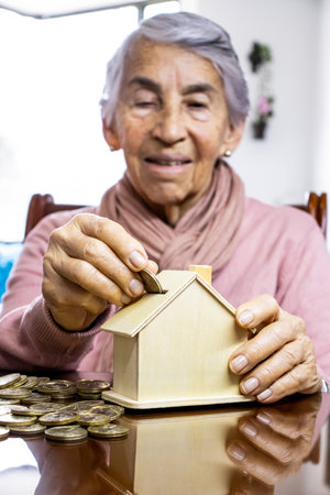 Closeup of a hand of a senior woman sitting at her home saving moneyの写真素材