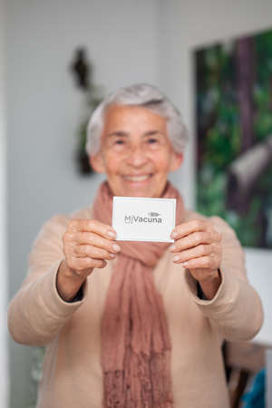 Senior woman at her home holding her vaccination certificate after getting the Covid-19 vaccine in Colombia. Authentic vaccination certificate. Real patientの写真素材