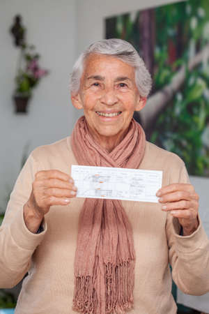 Senior woman at her home holding her vaccination certificate after getting the Covid-19 vaccine in Colombia. Authentic vaccination certificate. Real patientの写真素材