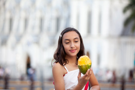 Beautiful tourist girl eating mango at the Ortiz Bridge with La Ermita church on background in the...