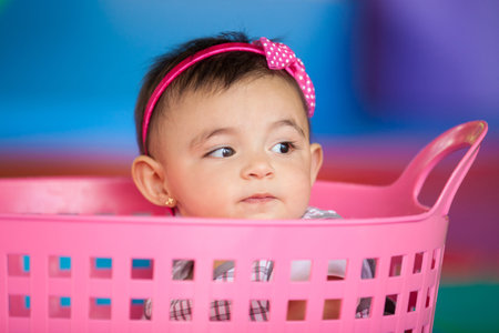 Beautiful ten months baby girl playing in a pink basket. Early stimulation for toddlers concept.の写真素材