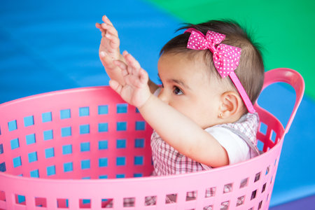 Beautiful ten months baby girl playing in a pink basket. Early stimulation for toddlers concept.の写真素材