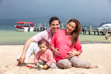 Young couple waiting for their second baby having fun with their baby girl at the beautiful white...