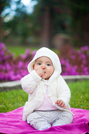 Sweet six months old baby girl sitting in the garden on a beautiful sunny day