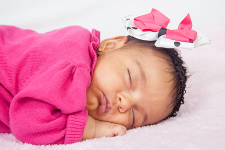 Closeup of a sweet little one month baby sleeping dressed in pink wearing a bowの写真素材