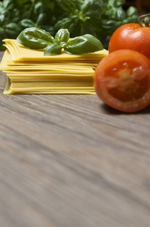 Raw pasta lasagna with basil leaves and fresh tomatoes on wooden backgroundの写真素材