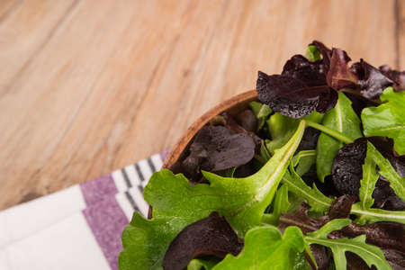 Fresh green salad with spinach, arugula, romaine and lettuce in a bowl on rustic wooden backgroundの写真素材