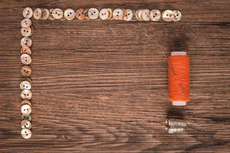 Sewing needle threaded with a orange thread ready for sewing. Buttons frame.の写真素材