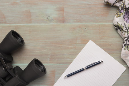 Close up binoculars, pen, paper and scarf on wooden table.