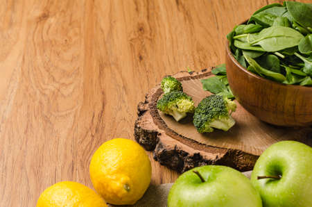 Spring spinach leaves in the bowl, broccoli, lemons and apples on wooden table backgroundの写真素材