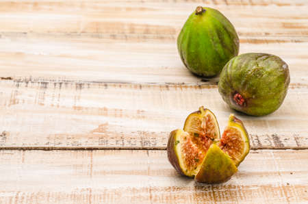 Whole figs and one fig sliced in half on top of a rustic wooden tableの写真素材
