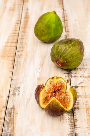 Whole figs and one fig sliced in half on top of a rustic wooden tableの写真素材
