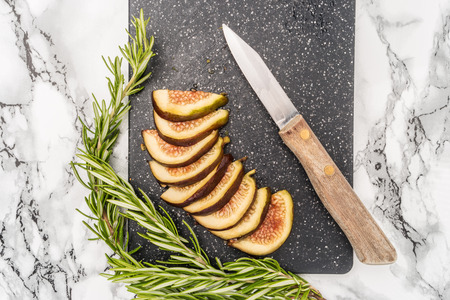 Fresh sliced figs, rosemary and knife on cutting board. Top viewの写真素材
