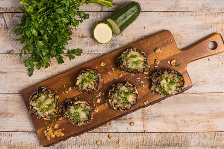 Mushroom caps stuffed with vegetables and cheese, baked in oven and garnished with a sprig of parsley. Mushroom appetizer on wooden board. Closeupの写真素材