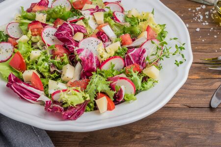 Fresh salad with mixed greens, radish, cheese and tomato in a plate on wooden background. Italian Mediterranean or Greek cuisine. Vegetarian vegan foodの写真素材