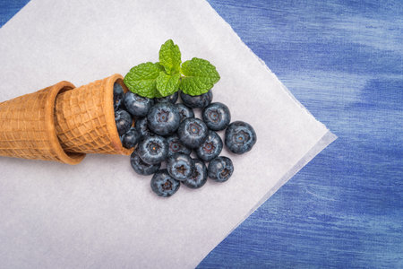 Waffle cones with blueberries and mint leaf on rustic textured background. Top view with copy space.の写真素材