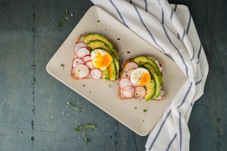 Sandwiches with avocado radish cheese and eggs on a rye bread on wooden board on dark background. Healthy breakfast. Vegetarian food.の写真素材