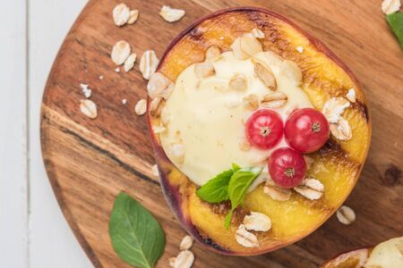 Grilled peaches with yogurt, gooseberries and mint leaves on wooden tableの写真素材