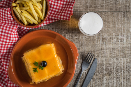Traditional Portuguese snack food. Francesinha sandwich of bread cheese pork ham sausages with tomato beer sauce and french fries. With a glass of beer and potatoes. On wooden table. Top view with copy spaceの写真素材