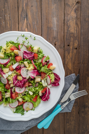 Fresh salad with mixed greens, radish, cheese and tomato in a plate on wooden background. Italian Mediterranean or Greek cuisine. Vegetarian vegan foodの写真素材