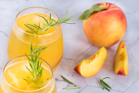 Homemade peach juice with ice cubes and rosemary leaves in glass on marble stone background.の写真素材