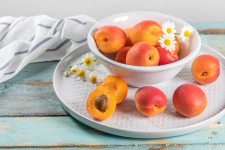 Delicious ripe apricots in a bowl on the wooden table. Close-up with apricots and daisy flowersの写真素材