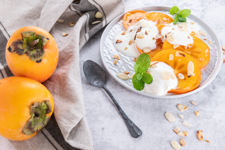 Sliced persimmon with yogurt and almonds. Healthy food concept on light backgroundの写真素材