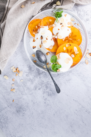 Sliced persimmon with yogurt and almonds. Healthy food concept on light background. top viewの写真素材