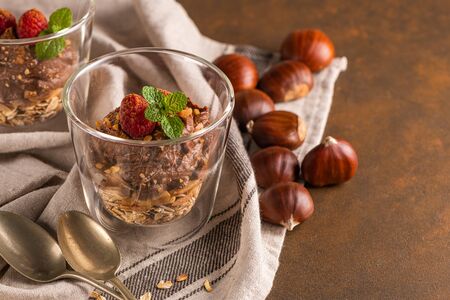 Glass cups of chocolate and chestnuts mousse with roasted almonds and oats decorated with raspberry and mint leaves.の写真素材