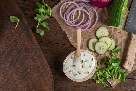 Top view of wooden cutting board on old wooden table top with tablecloth, sliced red onion and cucumber and corn saladの写真素材
