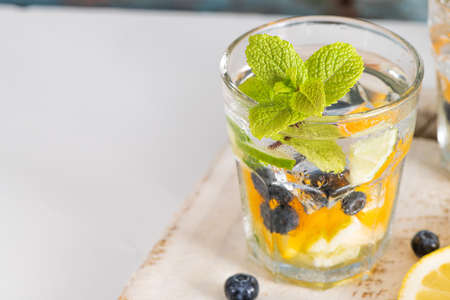 Summer healthy cocktails of citrus infused waters, lemonades or mojitos, with lime lemon orange blueberries and mint, diet detox beverages, in glasses on light backgroundの写真素材