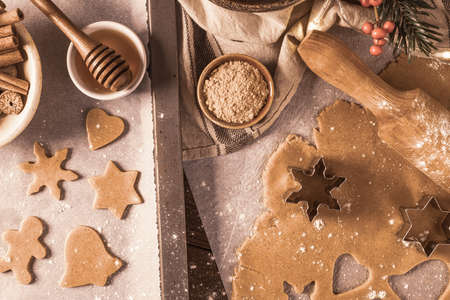 Making christmas gingerbread cookies. Raw dough in shape of gingerbread man, christmas tree, star, snowflakes on paper on tray on rustic table with rolling pin. Preparing for bakingの写真素材