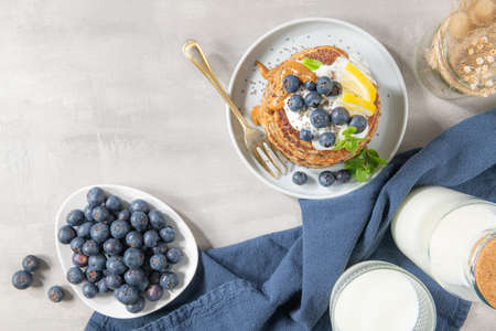 Healthy summer breakfast, homemade classic american pancakes with fresh blue berries, lemon, yogurt and peanut butter. Morning light grey stone background.の写真素材