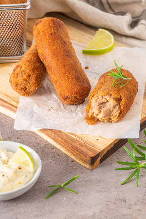 Meat croquets with garlic mayonnaise, lime slices to season and rosemary leaves on wooden table in a...