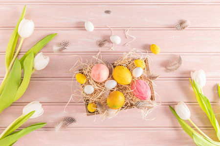 Easter pink, yellow and white eggs in wooden box and white tulips