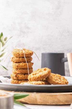 Stack of homemade oatmeal cookies, healthy breakfast cereal oat crackers and mug of milk with coffee...