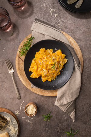 Farfalle pasta with pumpkin sauce and parmesan cheese decorated with rosemary on a black ceramic plate. Creamy cheesy vegan pumpkin paste. Kitchen counter top. Top view. flat layの写真素材