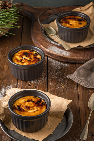 Creme brulee. Bowls with French vanilla cream dessert with caramelized sugar on top, spoons, dark rustic table. Cream milk, Portuguese desert similar to creme brulee, cream brulee and burnt cream.の写真素材