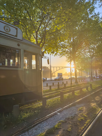 PORTO, PORTUGAL - CIRCA APRIL 2023: Wooden historical vintage yellow tram 287 moving on Porto street, symbol of city.Old tram passing by in Massarelos with the Arrabida bridge in the background during sunset. Indispensable transport for locals and interesのeditorial素材