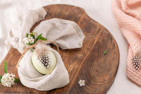 Stylish Easter brunch table setting with egg in easter bunny napkin. Modern natural dyed egg on...