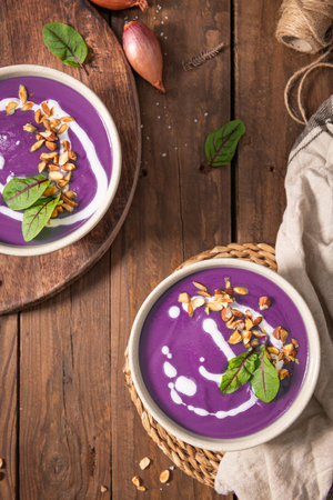 Red cabbage soup decorated with vegetables and pieces of toasted almonds on a rustic wooden board, accompanied by a spoon and shallots, creating a visually attractive and appetizing setting. Top viewの写真素材
