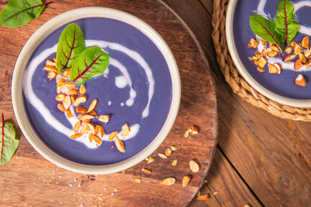 Red cabbage soup decorated with vegetables and pieces of toasted almonds on a rustic wooden board, accompanied by a spoon and shallots, creating a visually attractive and appetizing setting. Top viewの写真素材