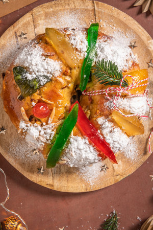 Colorful candied fruits and powdered sugar on a traditional Bolo Rei or Kings Cake, set on a wooden board amidst warm holiday decorations and lights. Is tradicional for Christmas in Portugal, Carnival or Mardi Gras. Top viewの写真素材