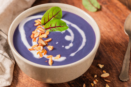 Healthy creamy red cabbage soup topped with herbs, a swirl of cream, toasted almonds, and fresh herbs, resting on a rustic wooden board.の写真素材