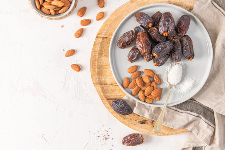 Medjool dates and almonds on a gray plate with a spoonful of shredded coconut, placed on a wooden...