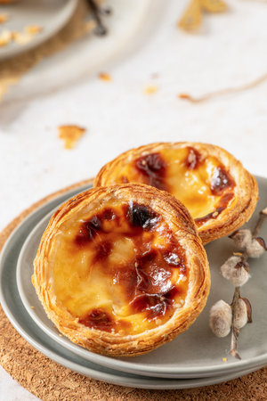 Two Portuguese custard tarts, pastel de nata, with caramelized tops on a gray plate, placed on a...