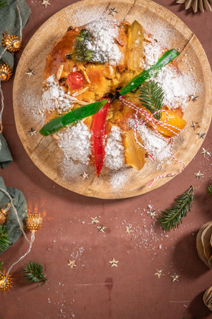 Colorful candied fruits and powdered sugar on a traditional Bolo Rei or Kings Cake, set on a wooden board amidst warm holiday decorations and lights. Is tradicional for Christmas in Portugal, Carnival or Mardi Gras. Top viewの写真素材